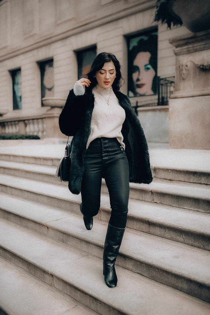 Bunette romanian blogger andreea cristina is walking down the art museum steps in downtown Chicago wearing a beige turtle neck, a gold necklace, a black faux fur jacket, highwaisted black jeans and mid calf black boots.